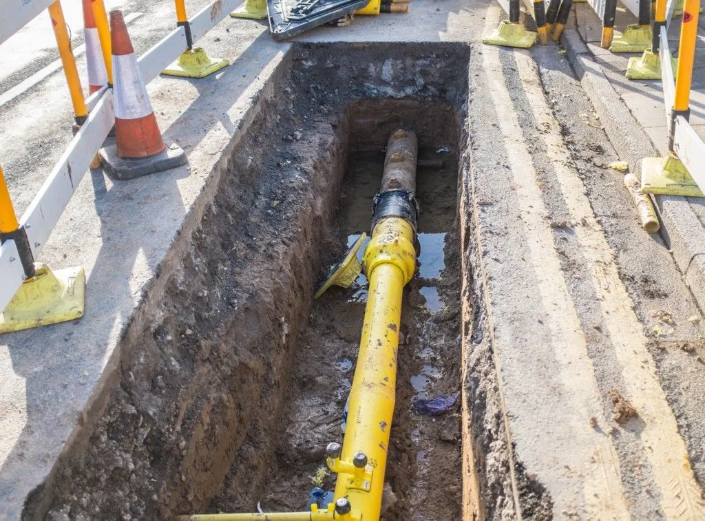 Yellow gas line being laid in an open trench beside a street