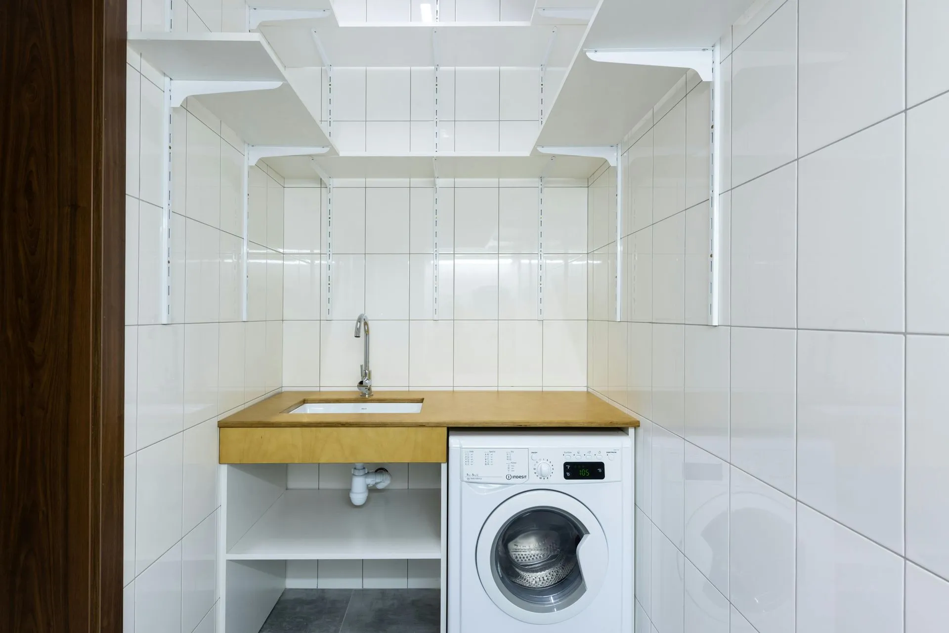 Tiled laundry room with a utility sink on a wood counter beside a front-load washer