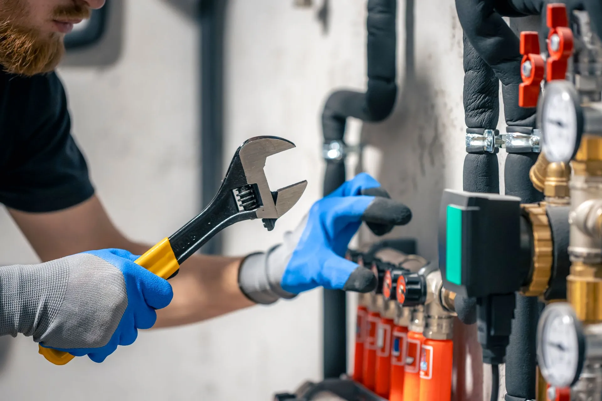 Plumber in blue gloves using an adjustable wrench on water valves and gauges