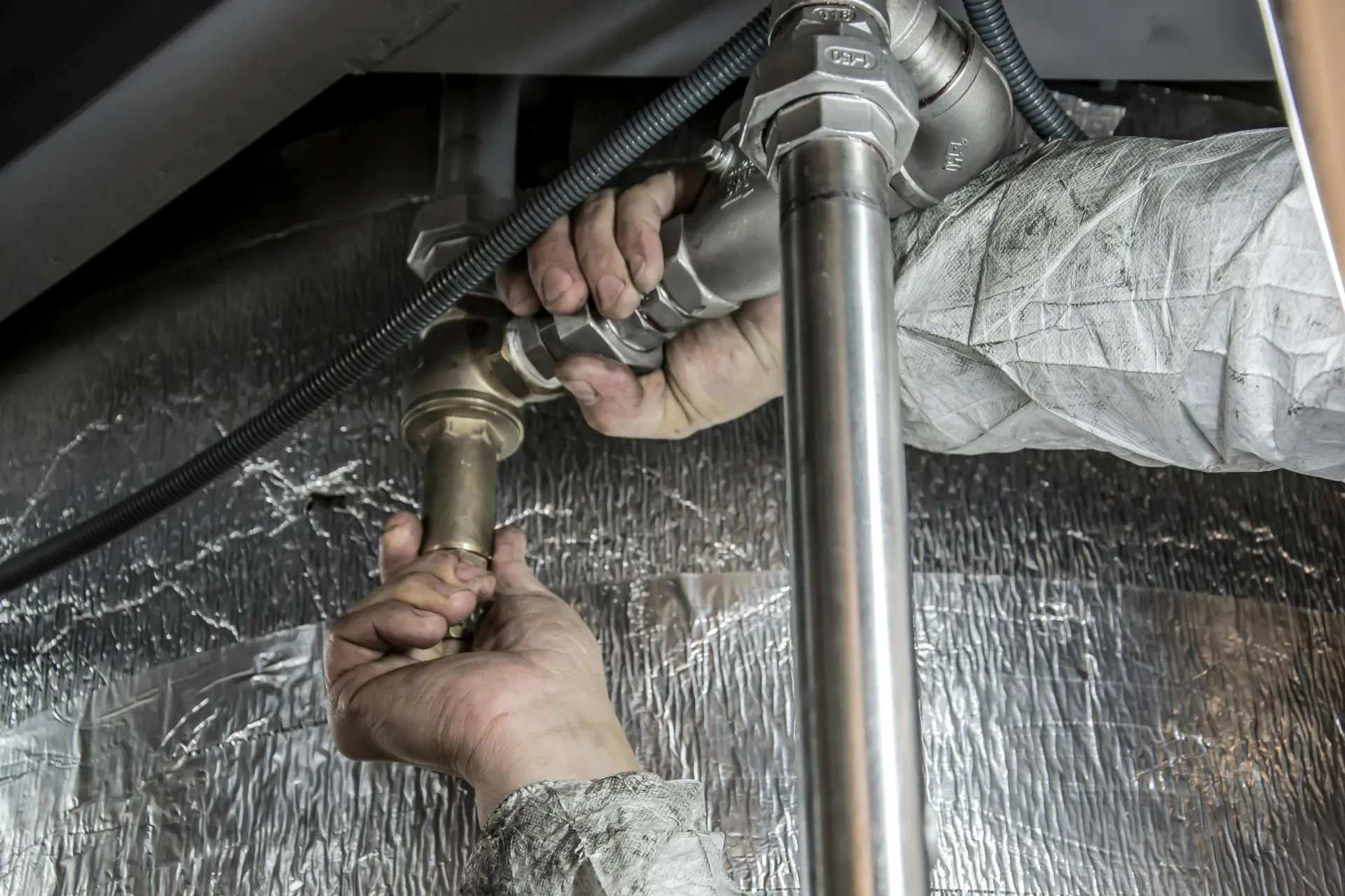 Plumber's hands connecting a steel water pipe fitting in a crawl space