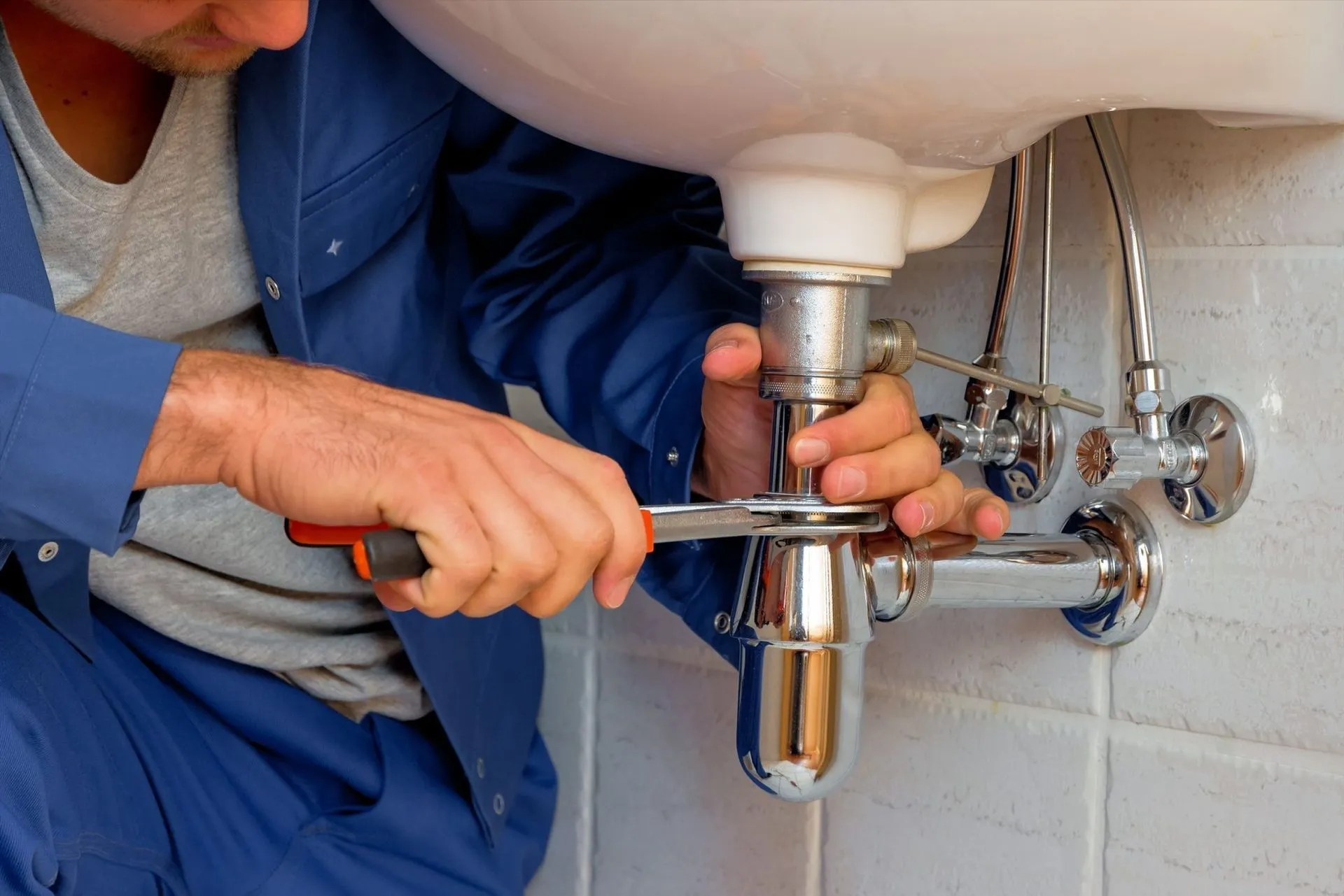 Plumber tightening a chrome P-trap under a bathroom sink with a wrench